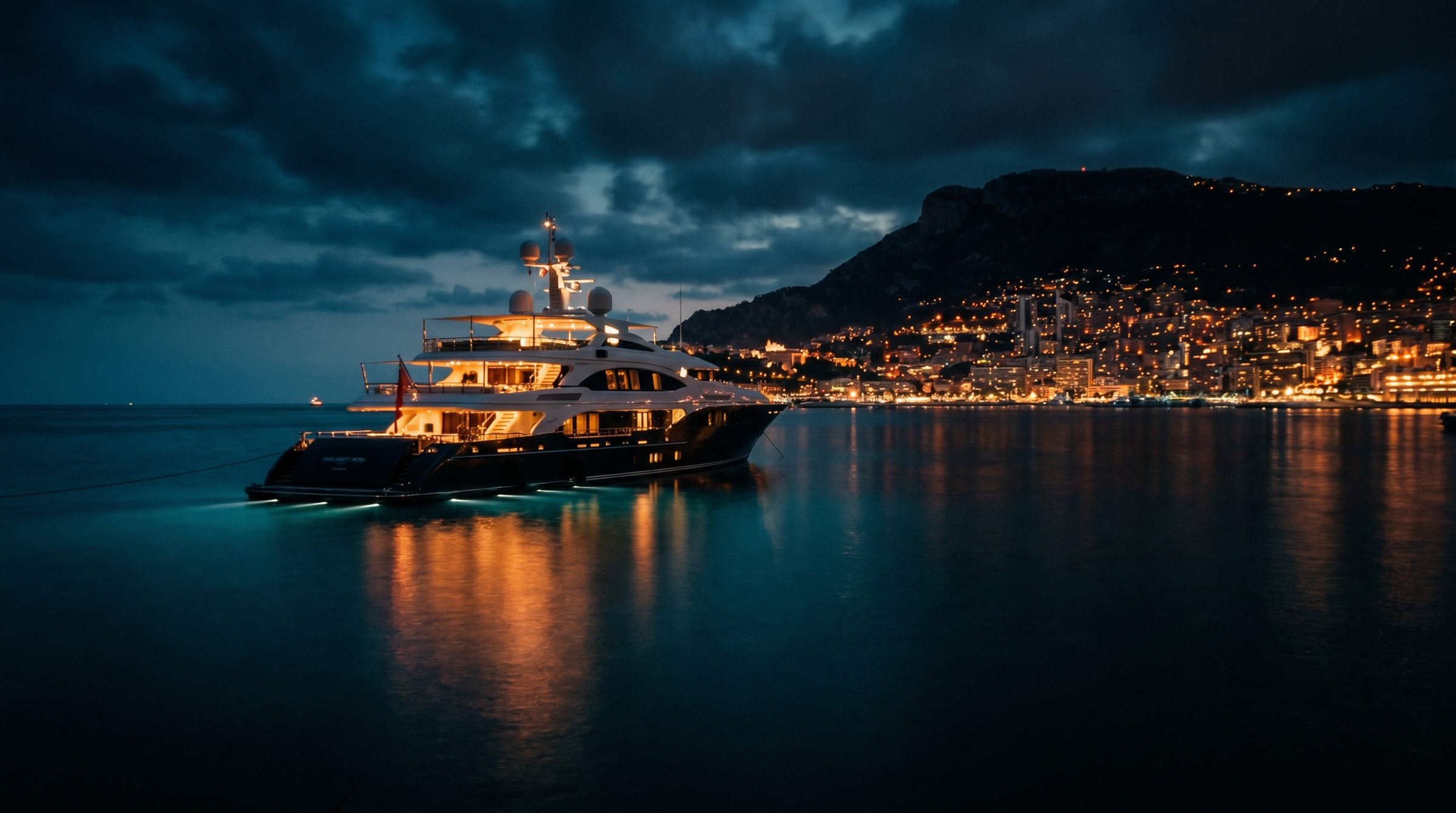 Superyacht moored against the lights of the Monaco coastline at night